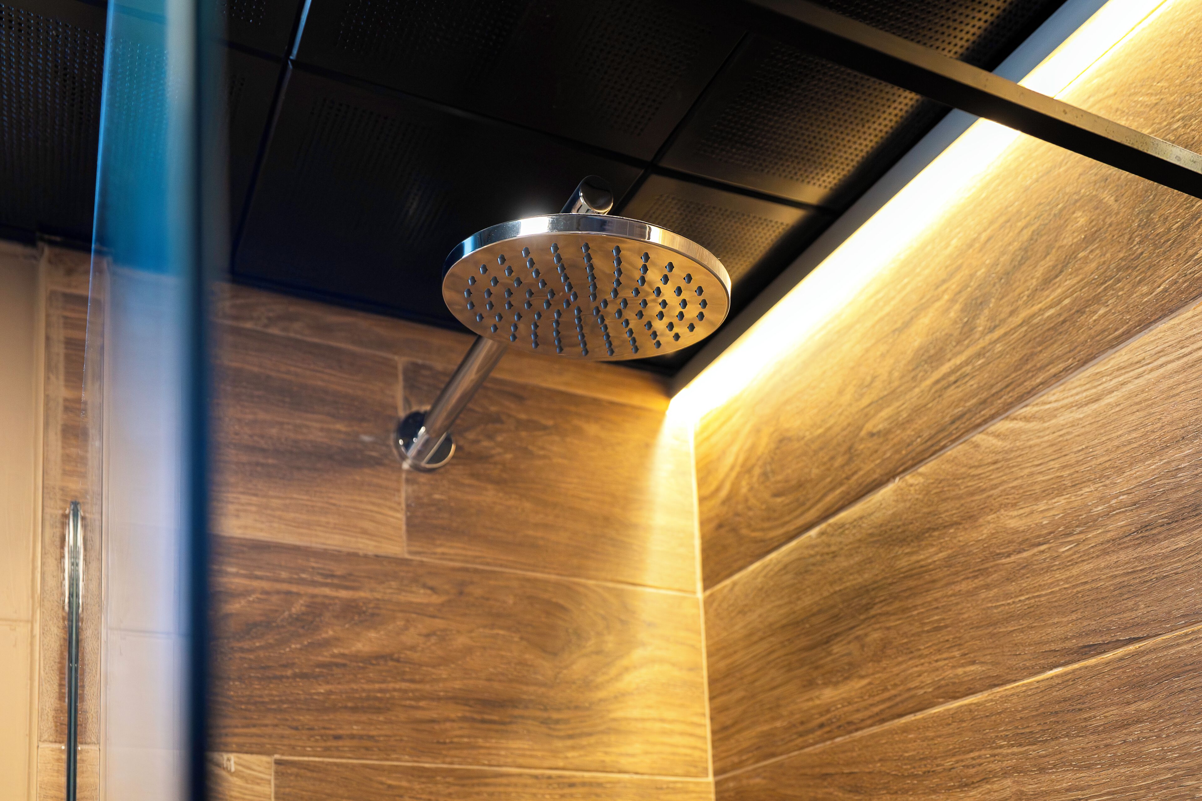 Een douchekop in een badkamer met houten wanden en een metalen fitting.
