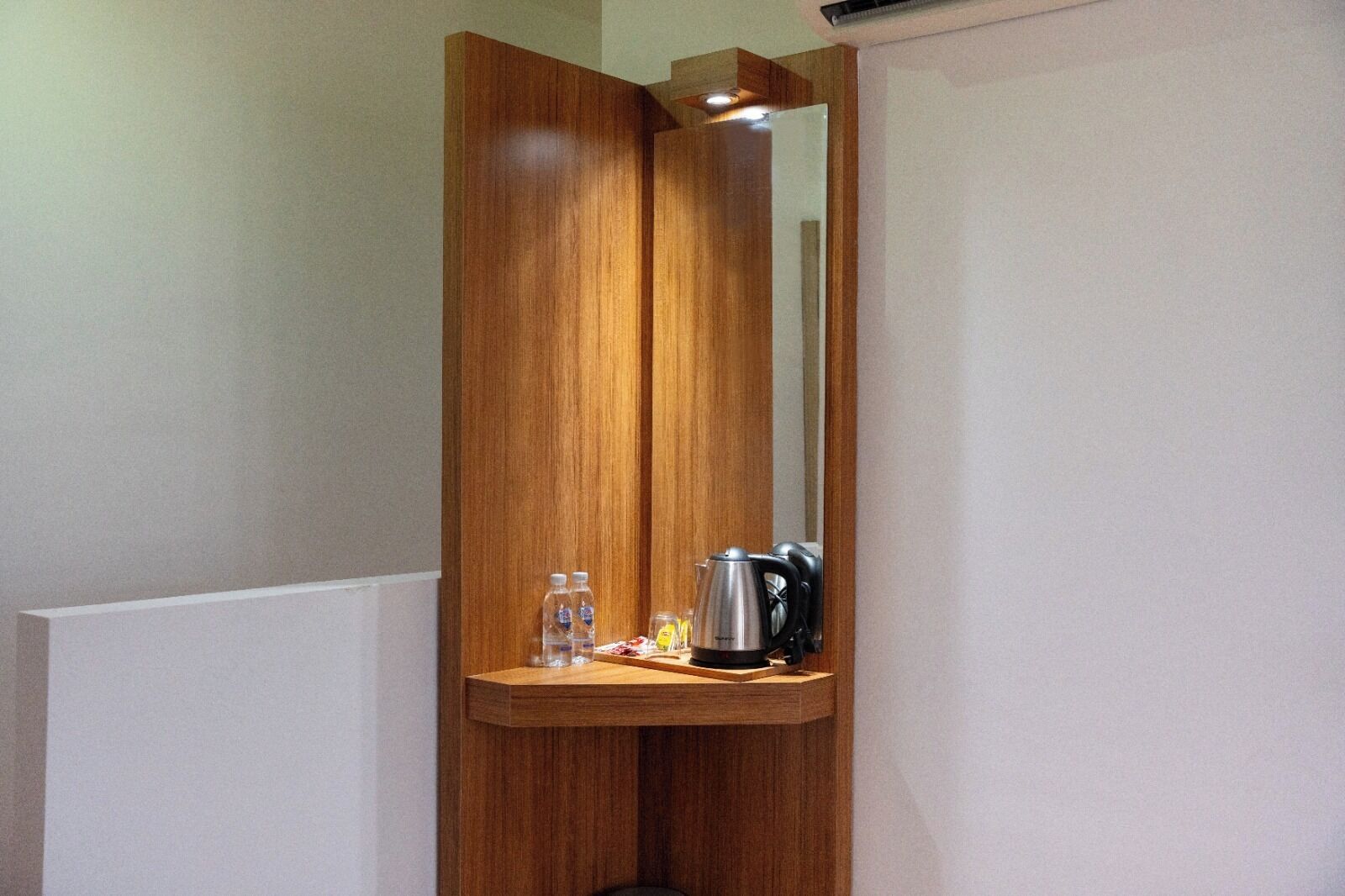 A wooden partition with a mirror, a shelf with a kettle, and two bottles.
