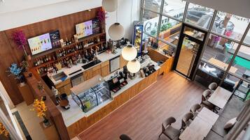 A modern bar area with a wooden counter, shelves of bottles, and a view of the street through large windows.