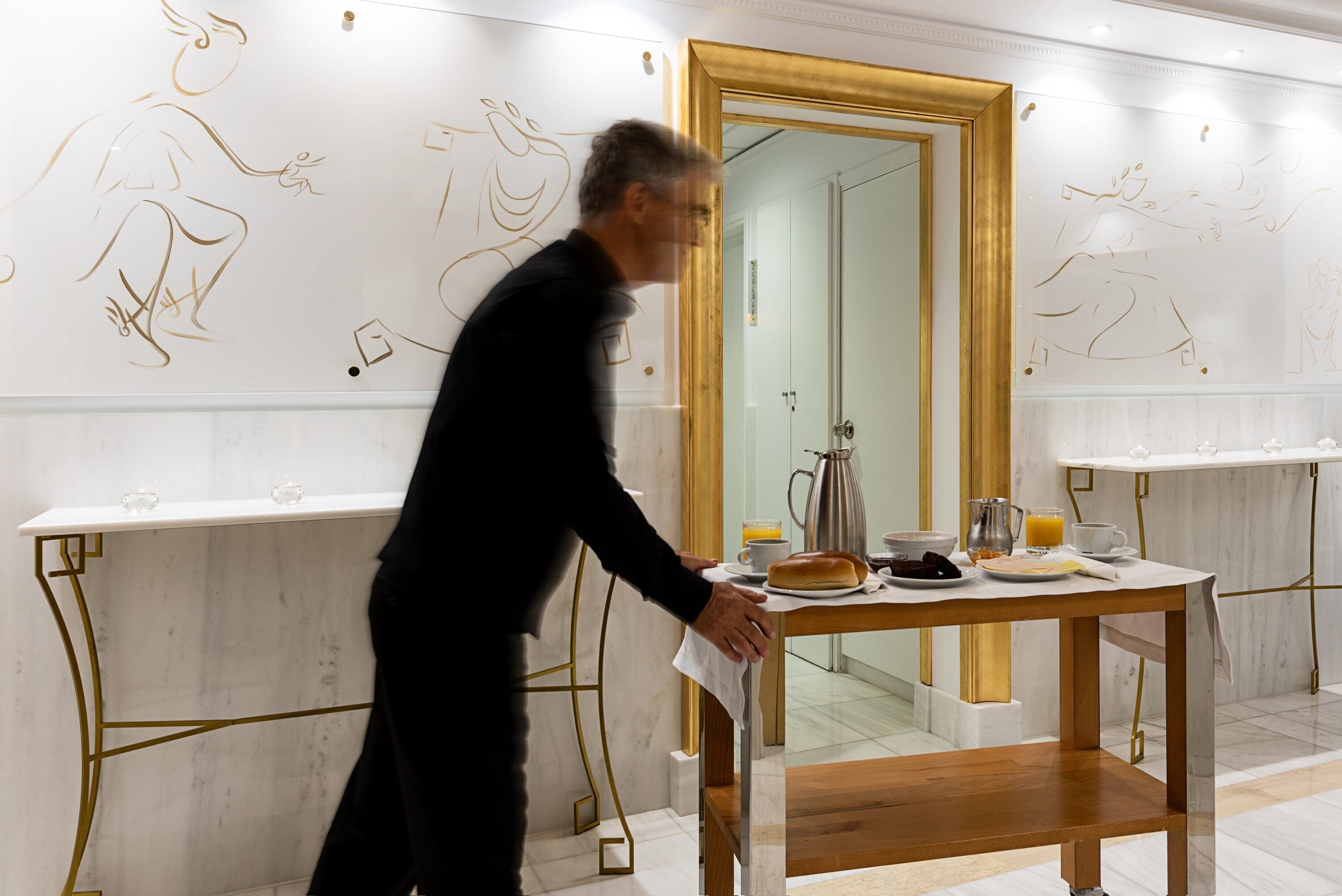 A modern hotel lobby with marble floors, a wooden reception desk, and a large mirror.