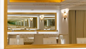 A hotel lobby with a large mirror reflecting the room, a seating area with tables and chairs, and a chandelier. - Hotel Galaxias (Rhodes)