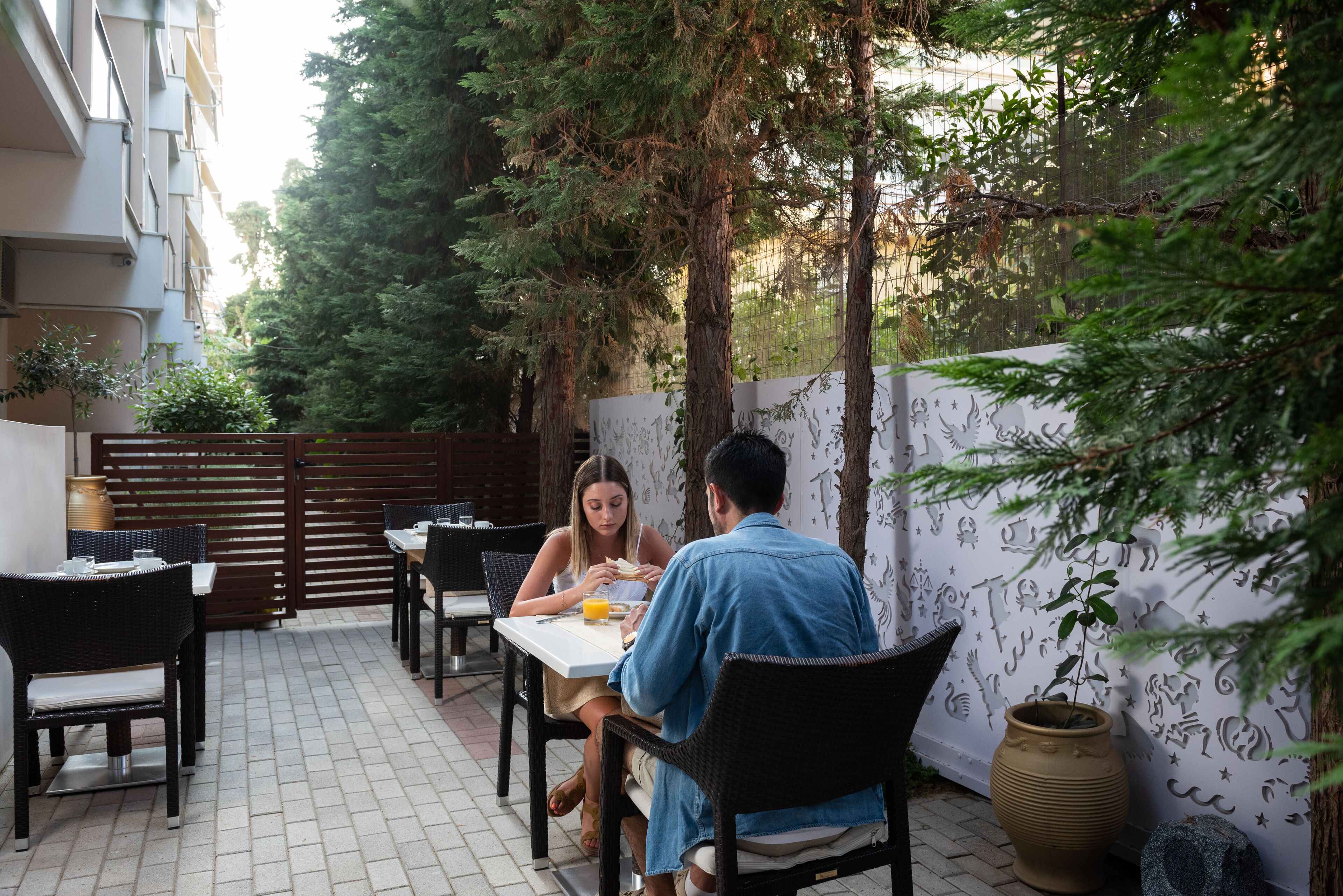 Un espace de restauration en plein air, avec des tables et des chaises, entouré de verdure et agrémenté d’un mur décoratif.