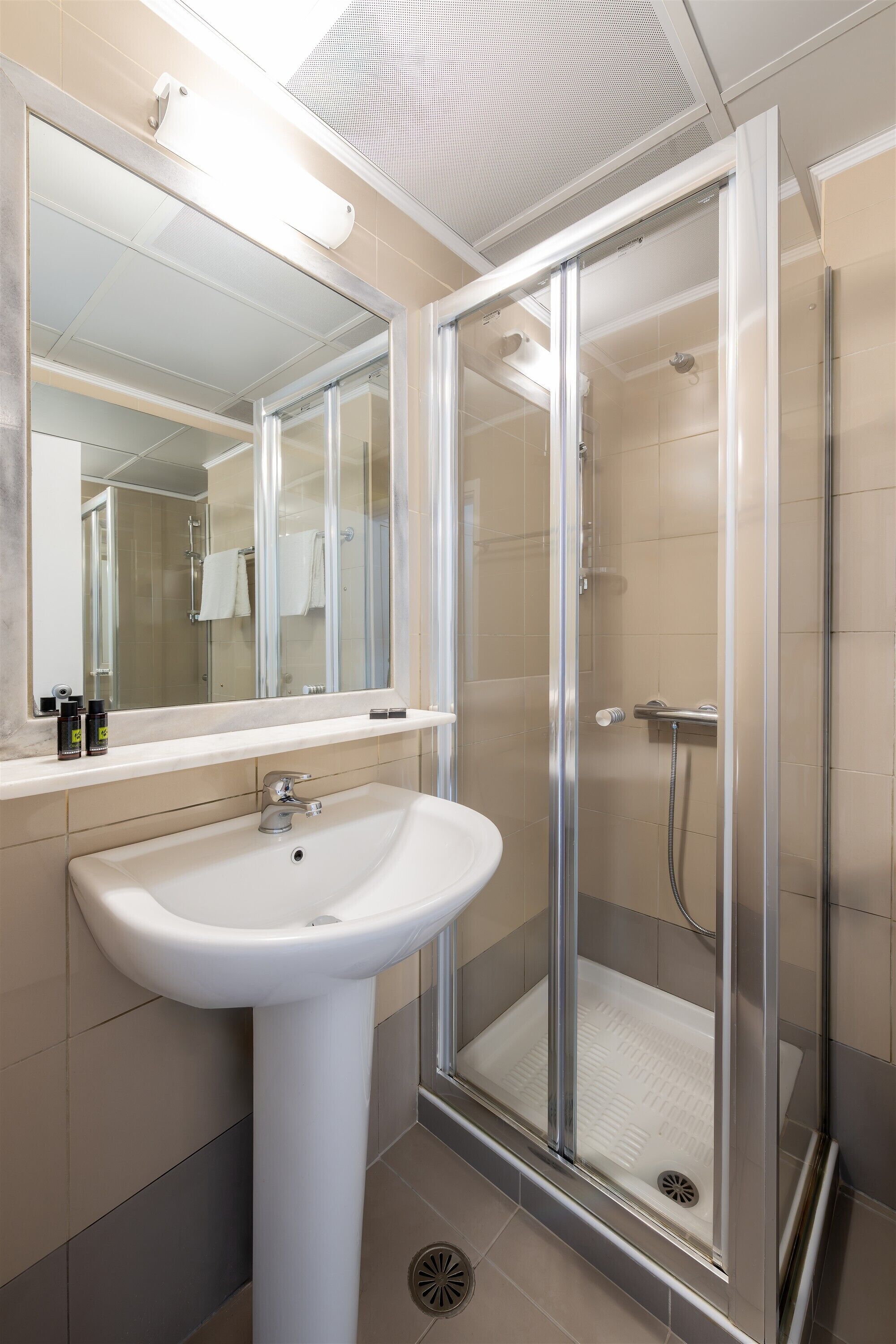 A modern bathroom with a glass-enclosed shower, a pedestal sink, and a mirror above the sink.