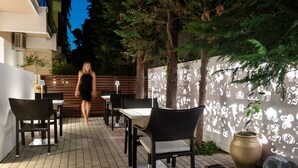 An outdoor patio area with wicker furniture, a large potted plant, and a decorative wall with cut-out designs. - Hotel Galaxias (Rhodes)