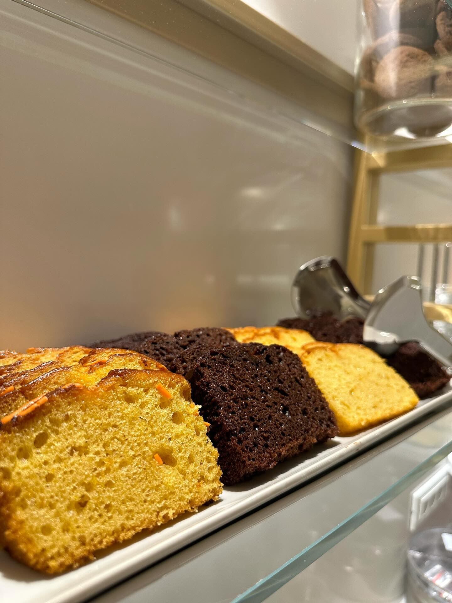Una bandeja con varios tipos de pasteles en una vitrina de vidrio.