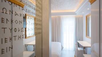 Ein Hotelzimmer mit einem Bett, einem Schreibtisch und einem Spiegel. An der Wand sind griechische Buchstaben angebracht und die Decke hat eine Leuchte.
