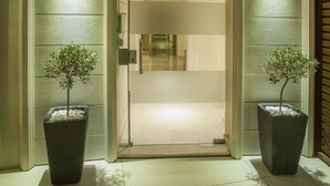 A modern entrance with a glass door, two potted plants, and a light fixture above. - Hotel Galaxias (Rhodes)