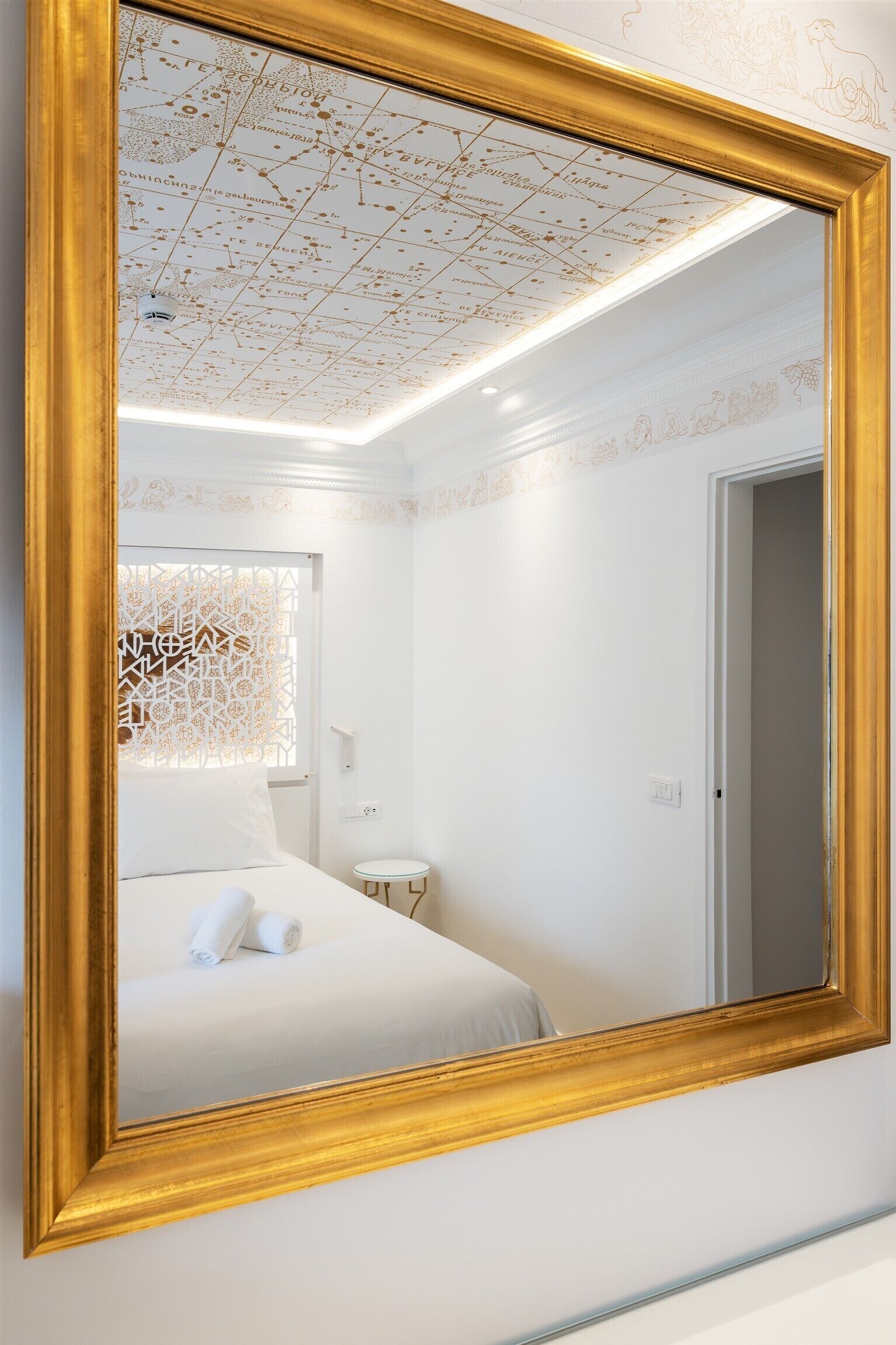 Un dormitorio con un espejo grande, una cama, una mesita de noche pequeña y un techo decorativo.