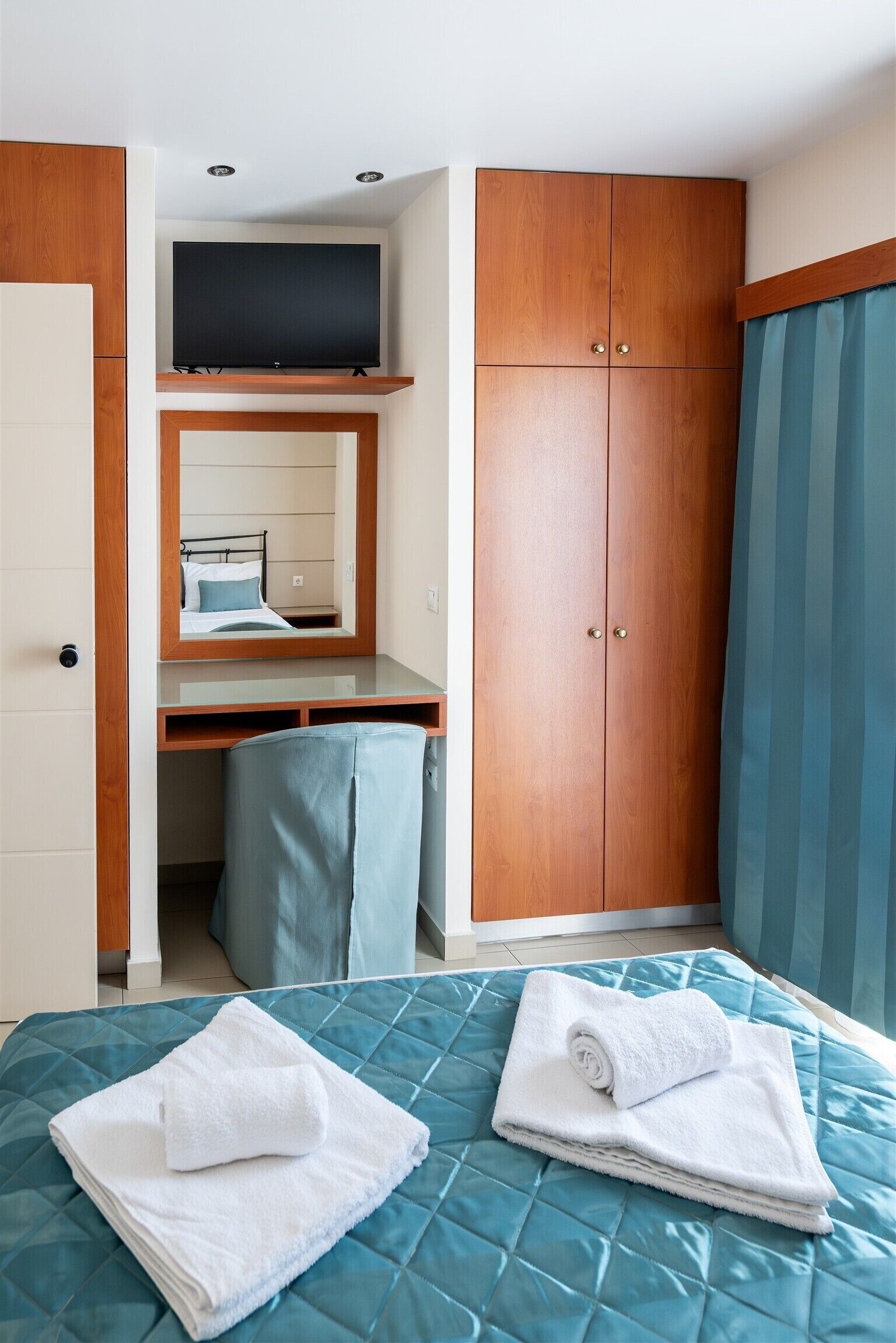 A hotel room with a bed, a desk with a mirror, a wardrobe, and a television.