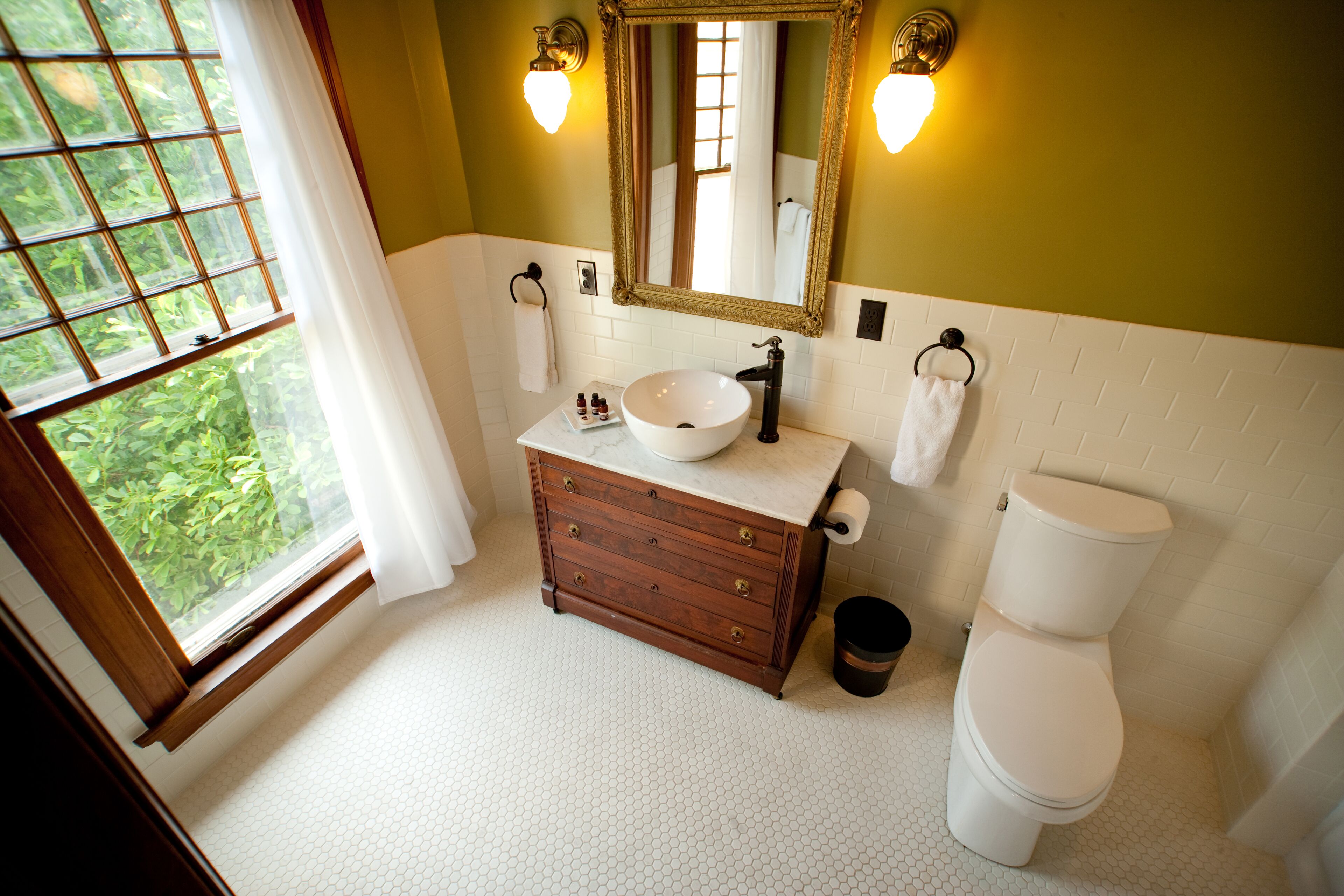 A bathroom with a wooden vanity, a white sink, a toilet, and a large mirror with wall sconces.