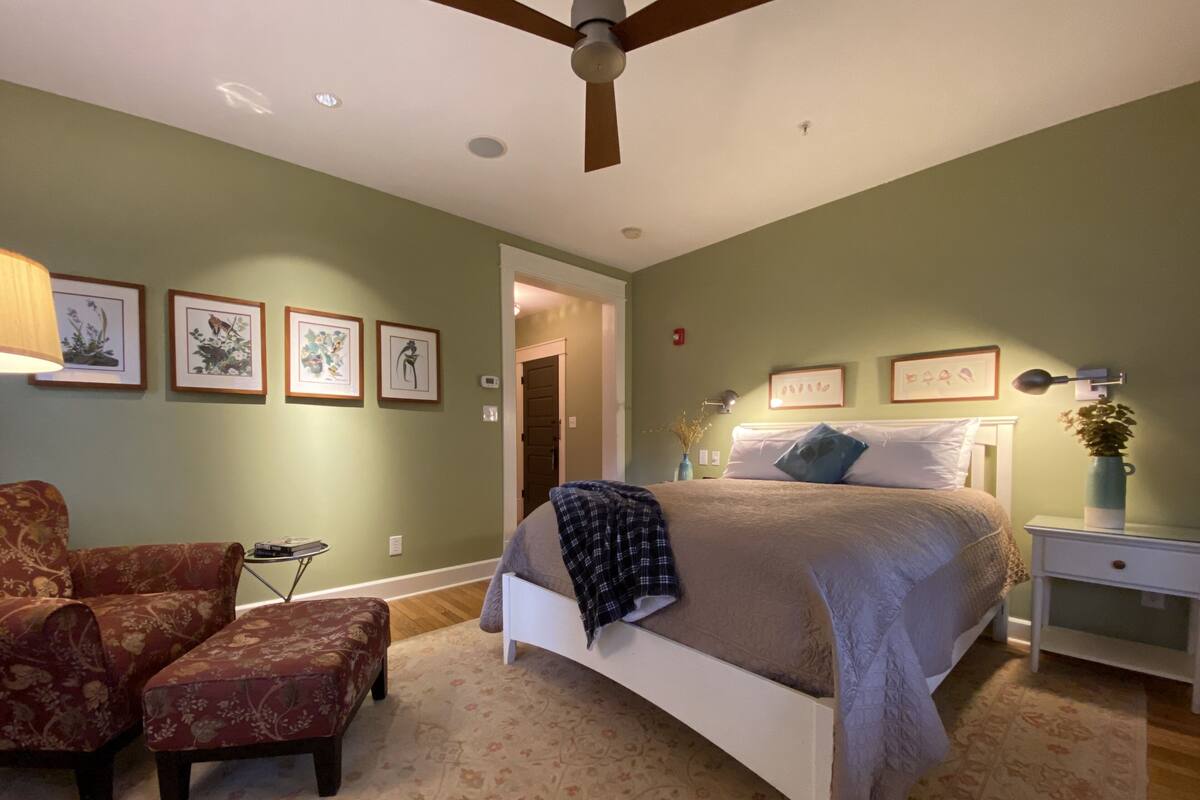 A bedroom with a bed, a chair, a nightstand, and framed pictures on the wall.