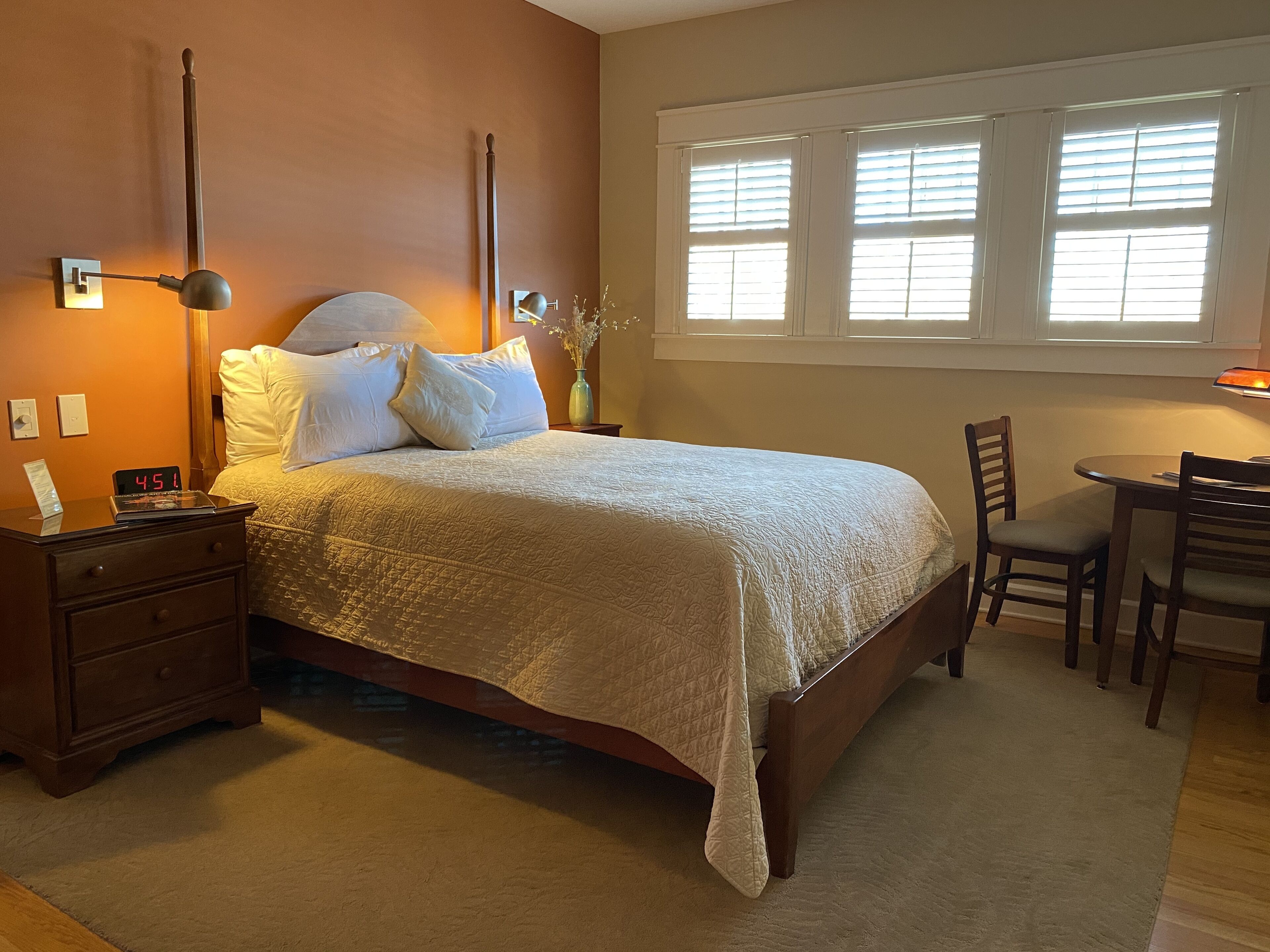 A neatly arranged bedroom with a bed, bedside table, lamp, and a small table with chairs.