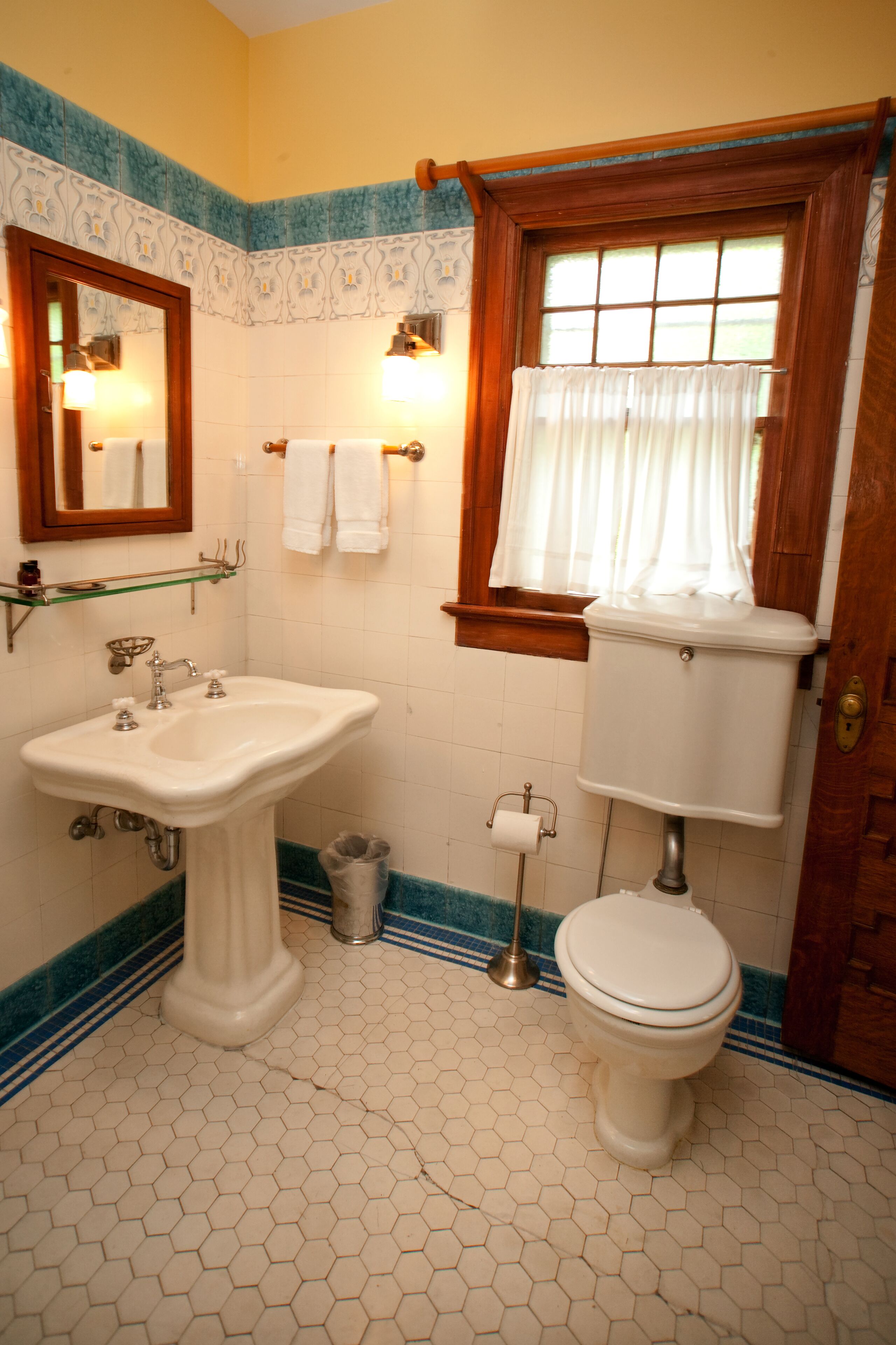 Un bagno con un lavabo a piedistallo, un water e una finestra con tende.