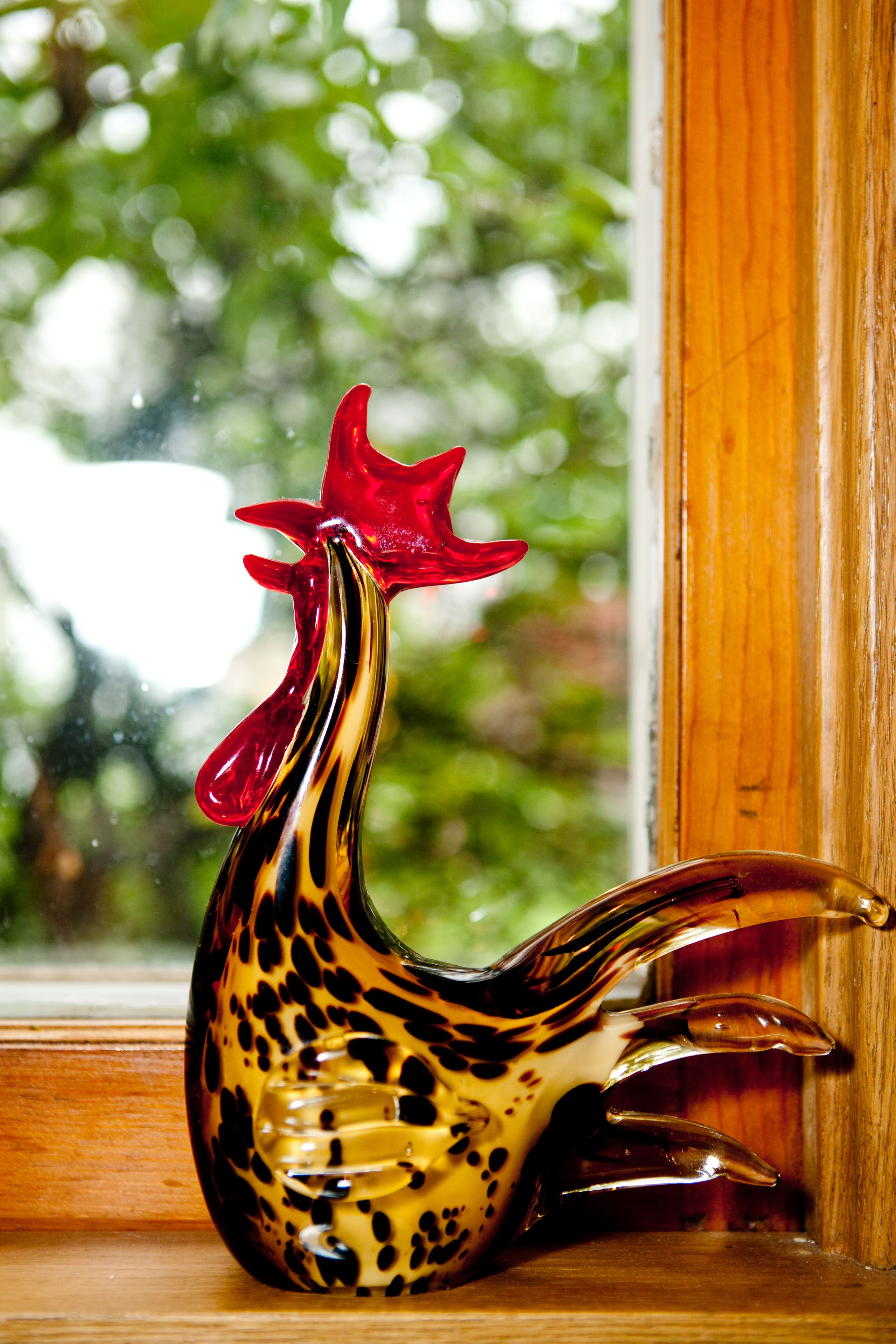 A ceramic rooster figurine placed on a wooden ledge by a window.