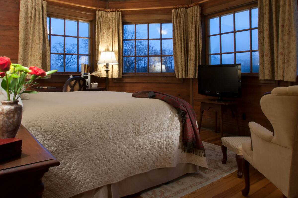 A cozy room with a large bed, a television, and a window with curtains.