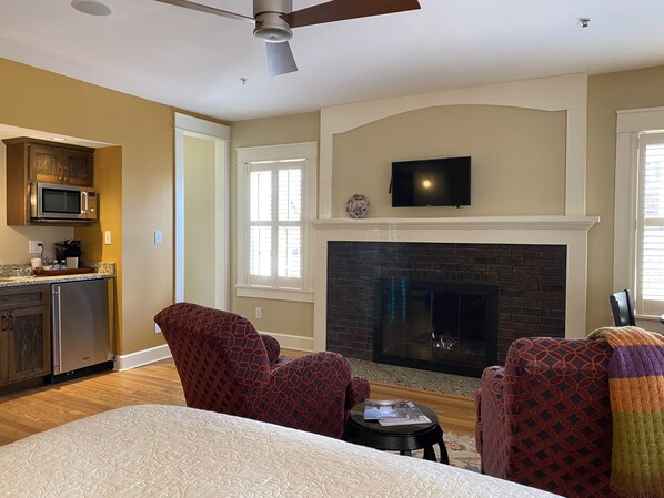 A living room with a fireplace, a television mounted above it, and a kitchen area with a microwave and refrigerator.