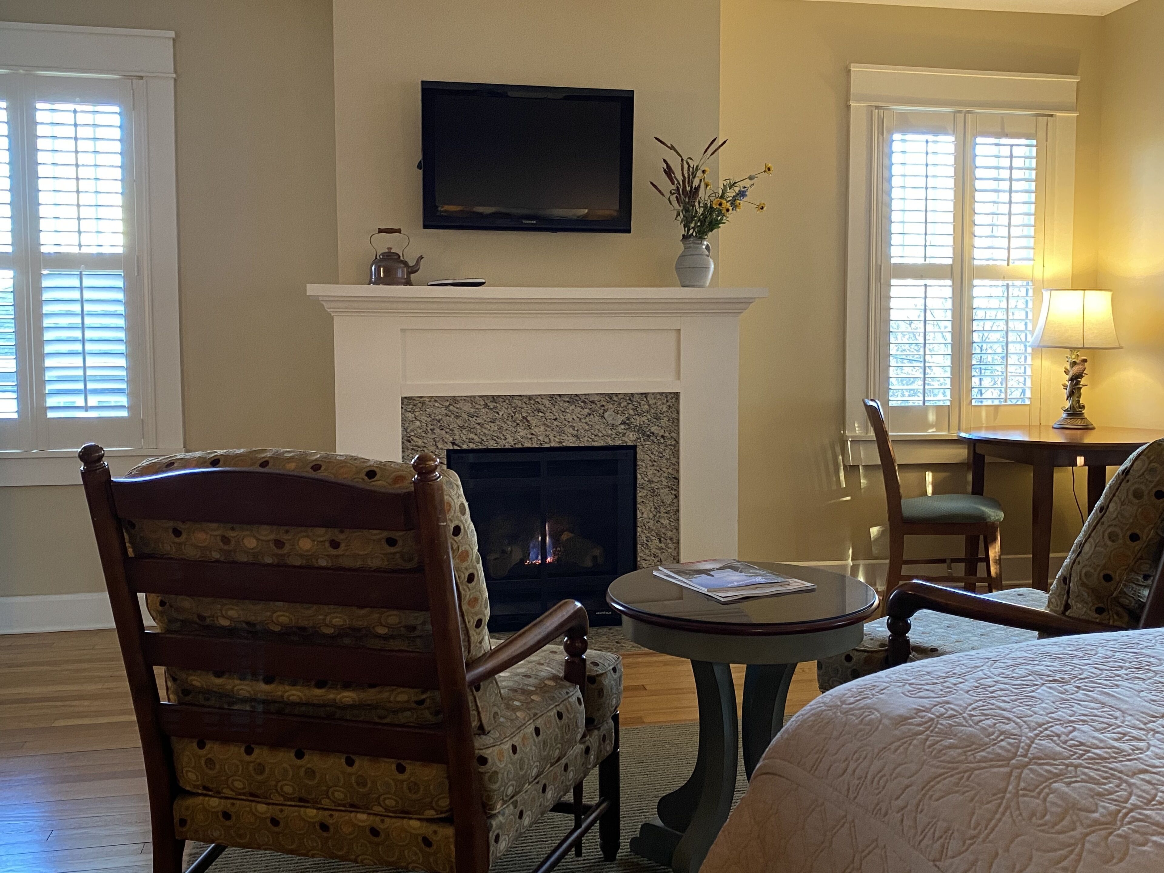 A cozy room with a fireplace, a television mounted above it, and a comfortable seating area with a chair and a table.