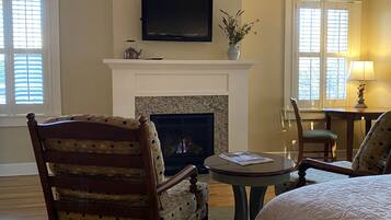 A cozy room with a fireplace, a television mounted above it, and a comfortable seating area with a chair and a table.