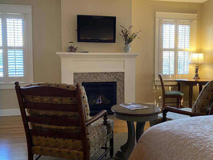 A cozy room with a fireplace, a television mounted above it, and a comfortable seating area with a chair and a table.