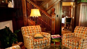 Una sala de estar acogedora con sillones estampados, una mesa de centro de vidrio y una escalera al fondo.