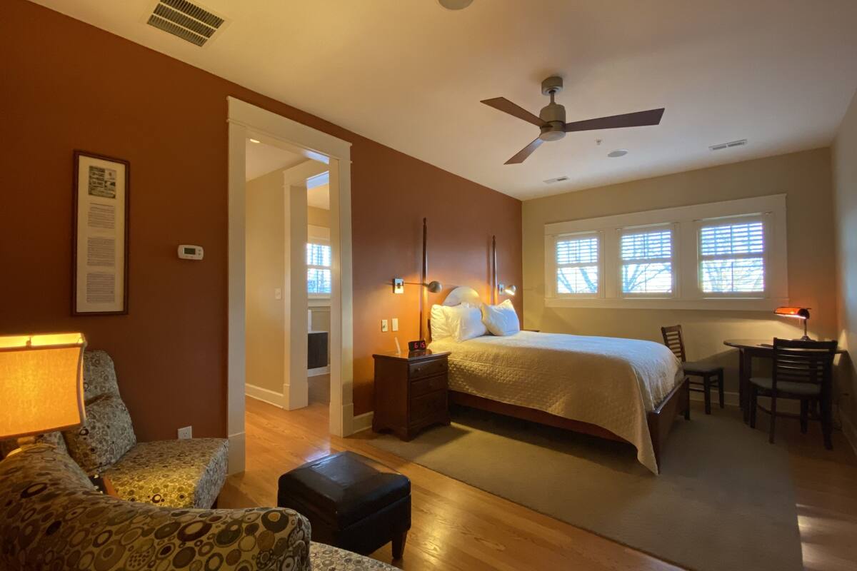 A bedroom with a bed, a desk, a chair, a lamp, and a ceiling fan.