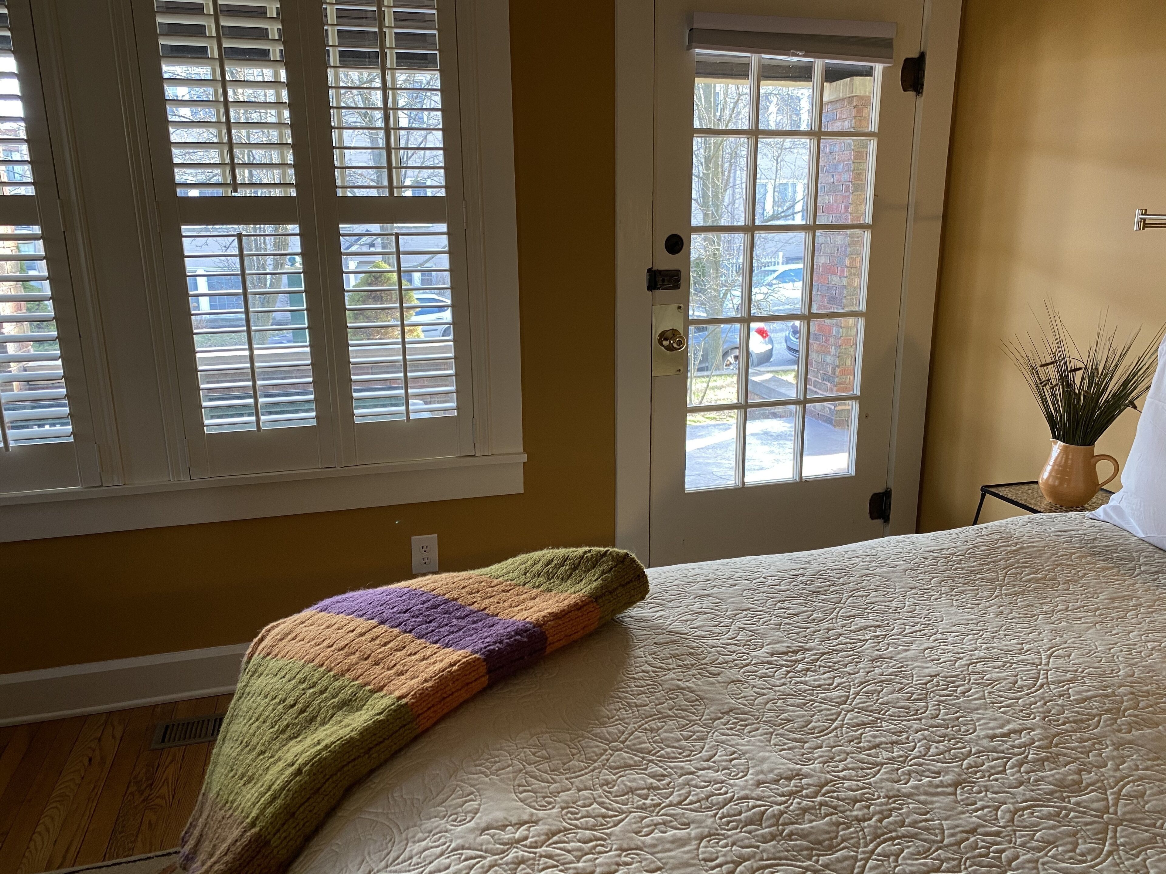 Un dormitorio con una cama, una puerta con ventana y una pequeña mesa con una planta.