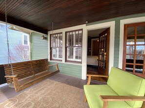 A porch with a wooden bench, a green cushioned chair, and a patterned rug.