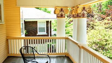 A covered porch with two chairs, a ceiling fan, and a view of a house and garden.
