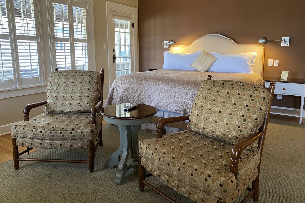 A hotel room with a bed, two armchairs, a small table, and a nightstand.