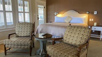 A hotel room with a bed, two armchairs, a small table, and a nightstand.