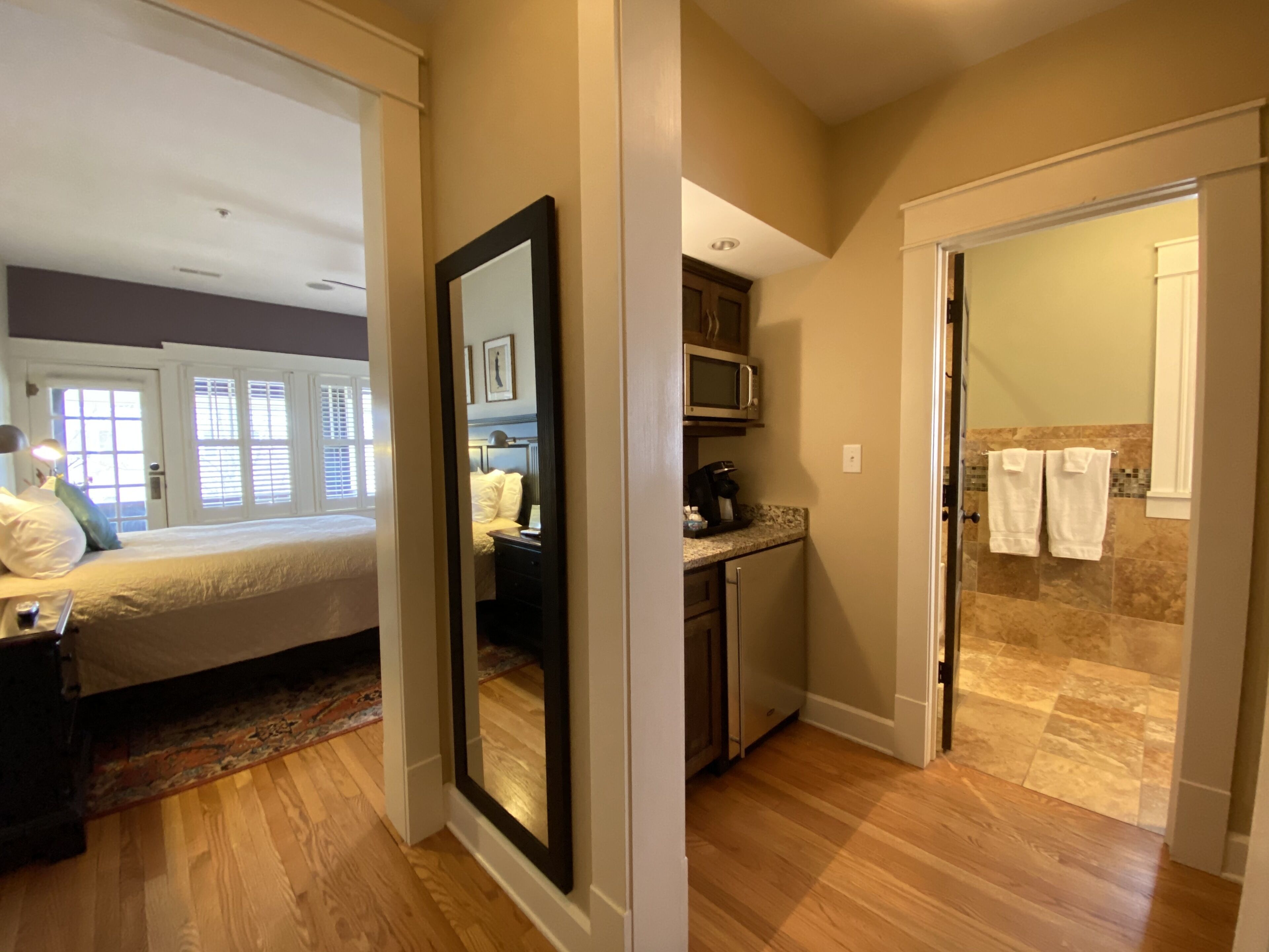 Habitación de hotel con cama, escritorio, espejo, kitchenette y baño con ducha y toallas.