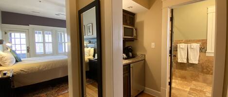 Habitación de hotel con cama, escritorio, espejo, kitchenette y baño con ducha y toallas.