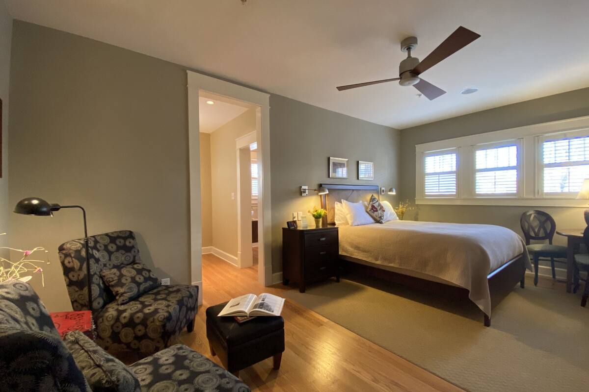 A bedroom with a bed, a desk, a chair, a lamp, and a ceiling fan.