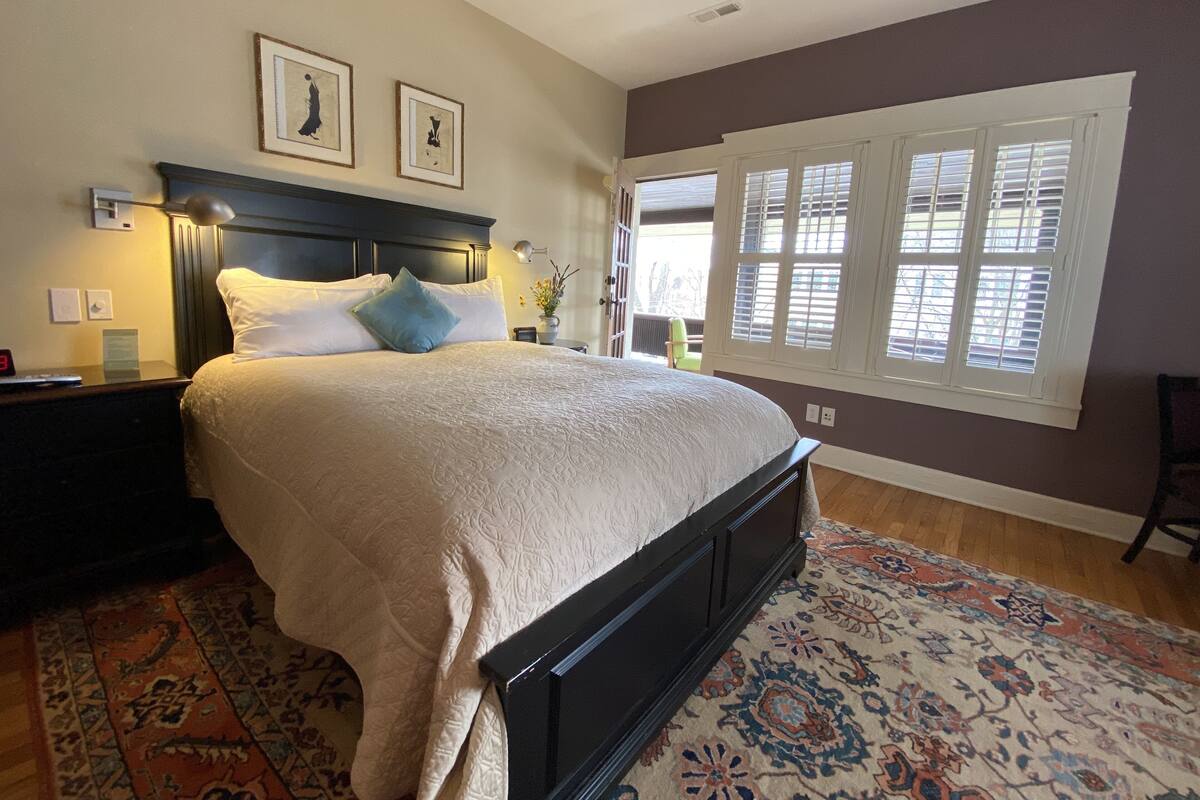 A neatly made bed with a headboard, a bedside table with a lamp, and a window with blinds.