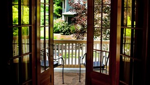 Puerta de madera que da a un patio exterior con dos sillas y una valla blanca.