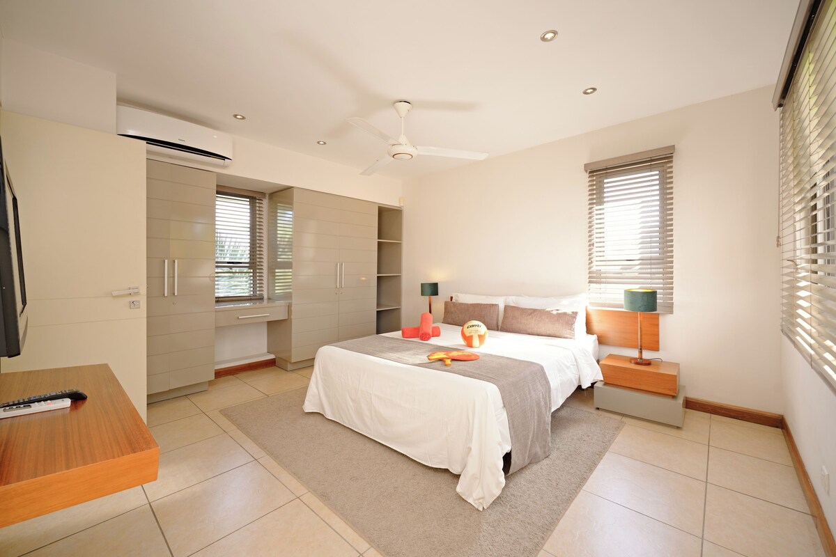 A bedroom with a bed, bedside tables, a ceiling fan, and a window with blinds.