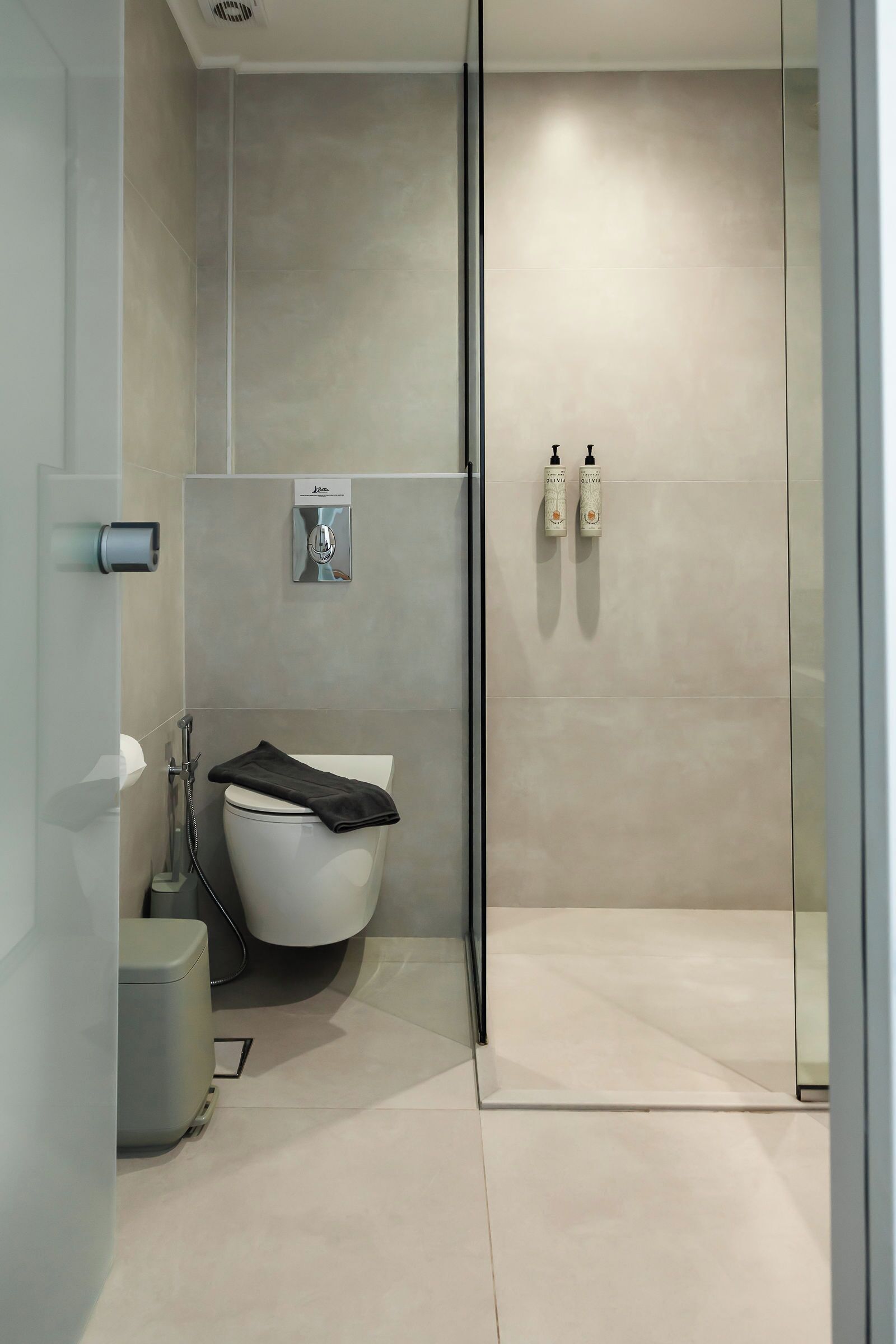 A modern bathroom with a glass shower enclosure, a toilet, and two hand soap dispensers mounted on the wall.