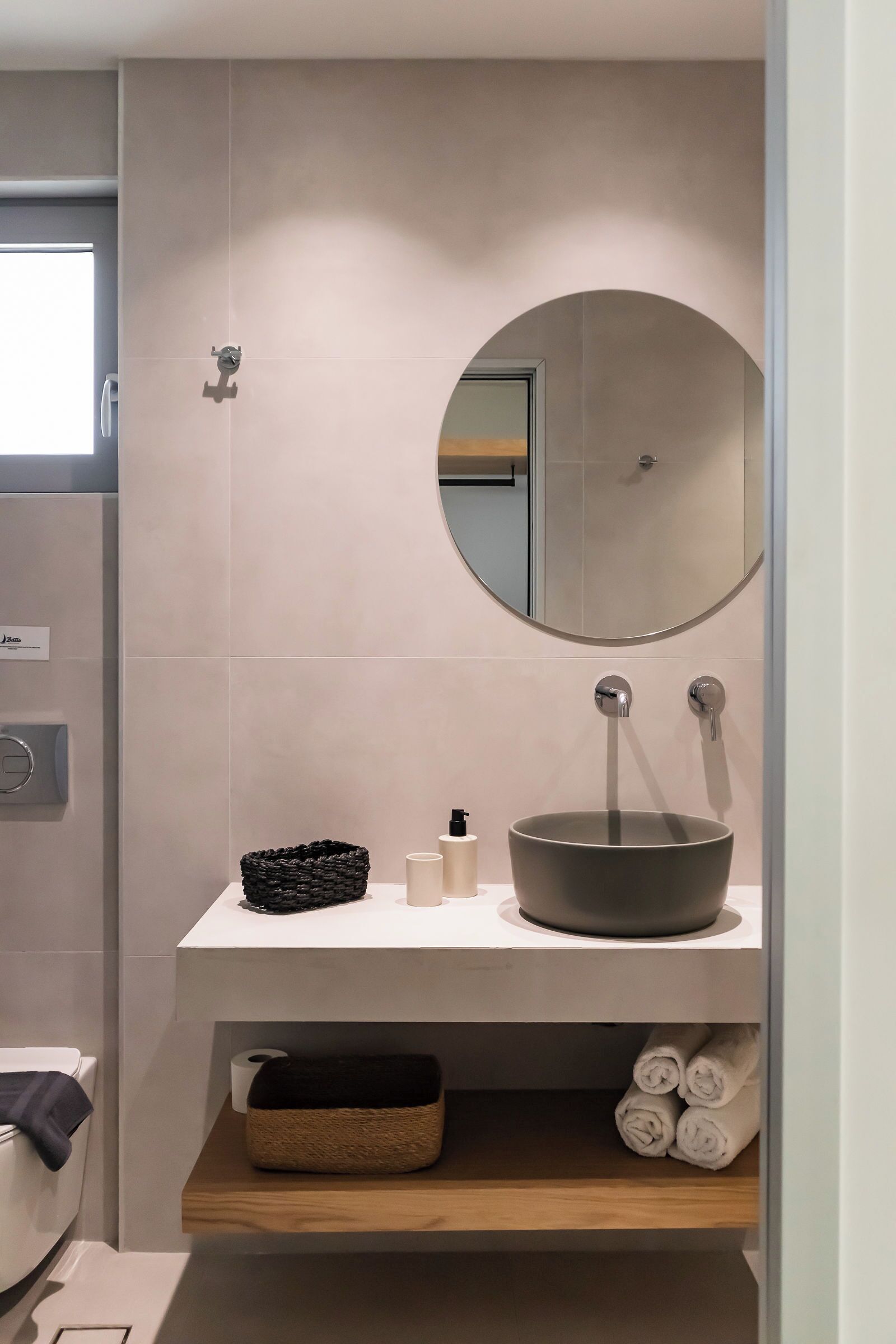 Un baño moderno con un espejo redondo, un lavabo y un perchero para toallas.