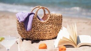 Escena de playa con un bolso tejido, un libro y una manta.