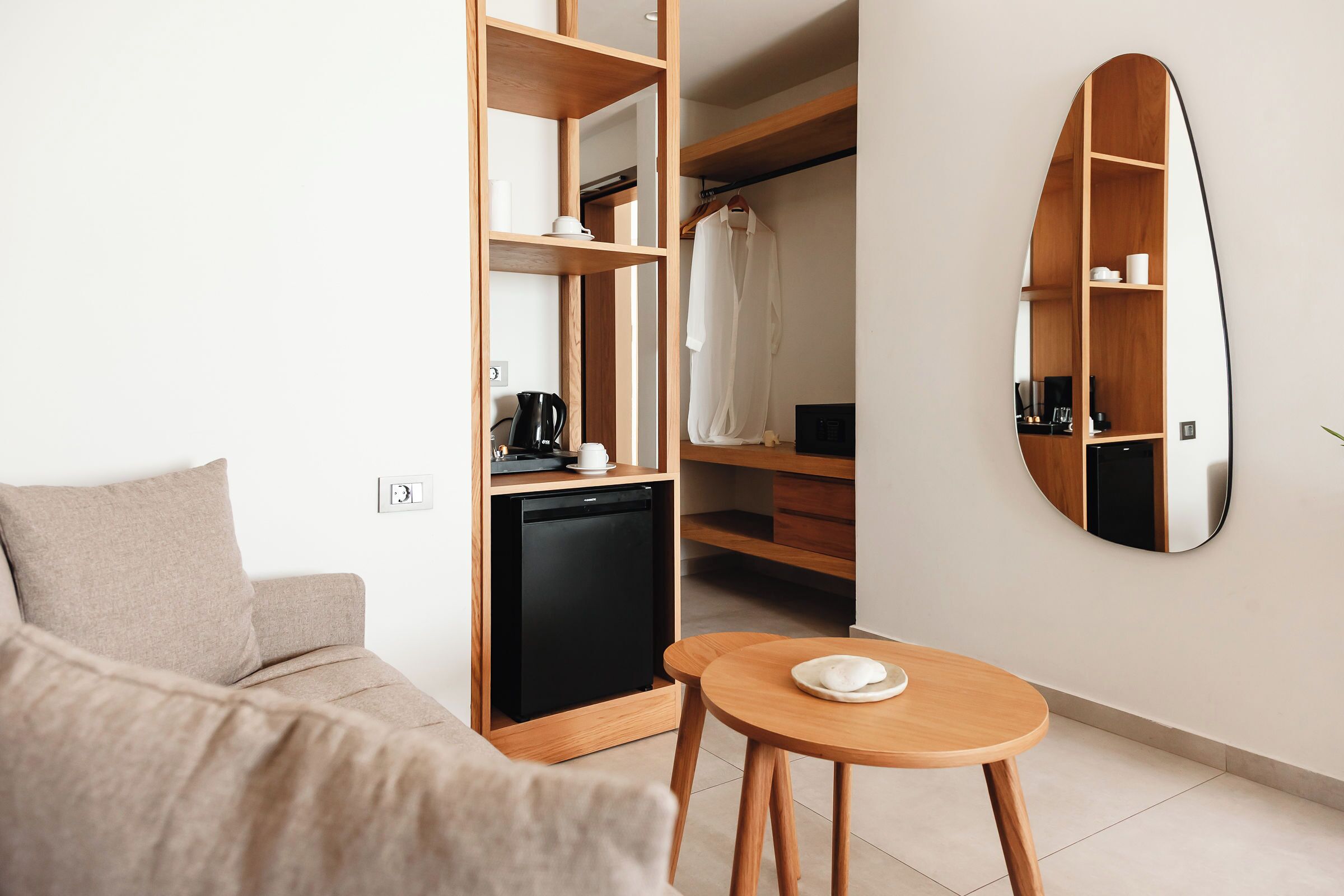 Ein modernes Hotelzimmer mit einer Couch, einem kleinen Tisch, einer Kaffeemaschine, einer Minibar und einem Kleiderschrank mit Spiegel.