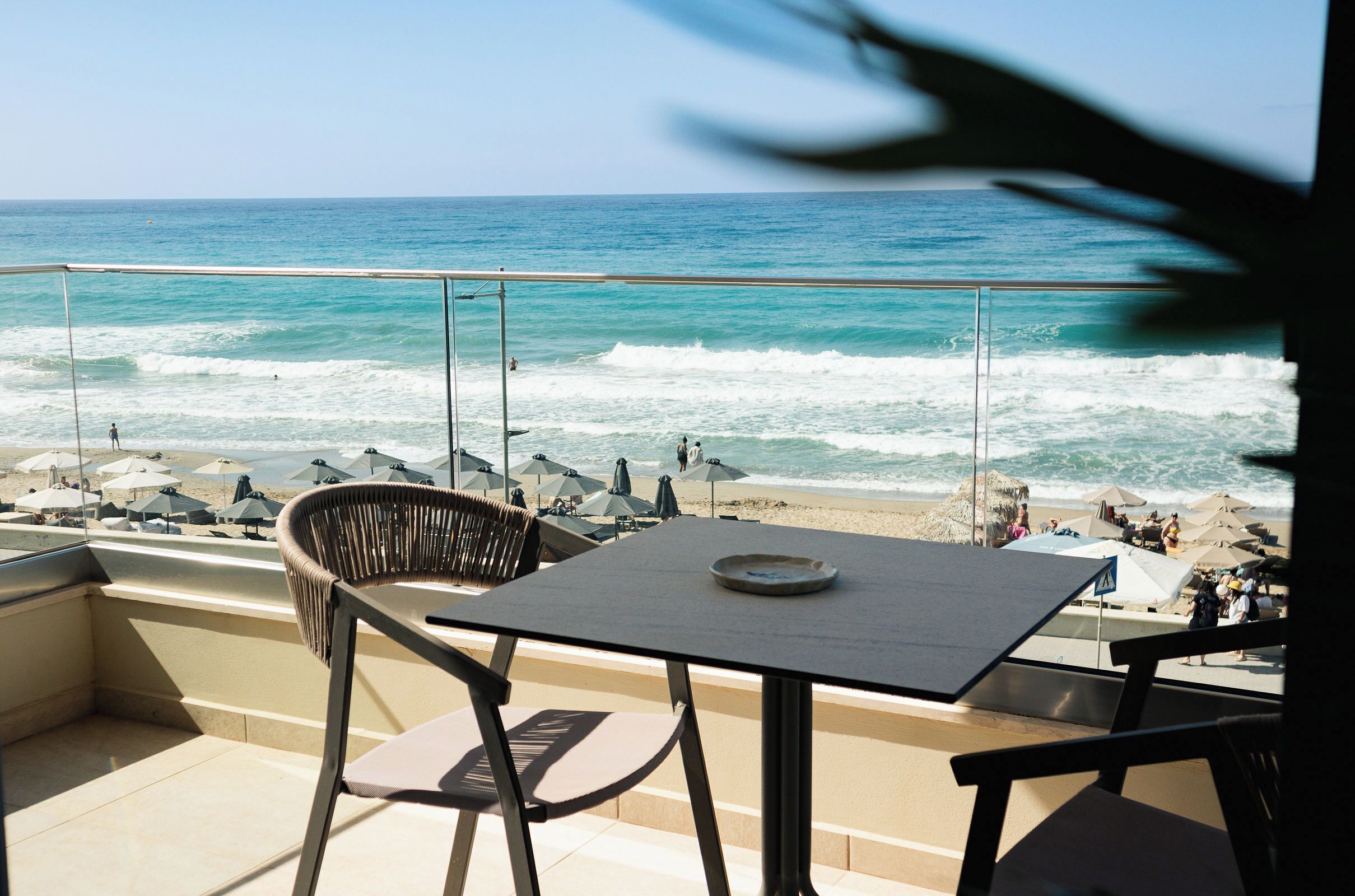 A balcony with a table and chairs overlooking the beach and ocean.
