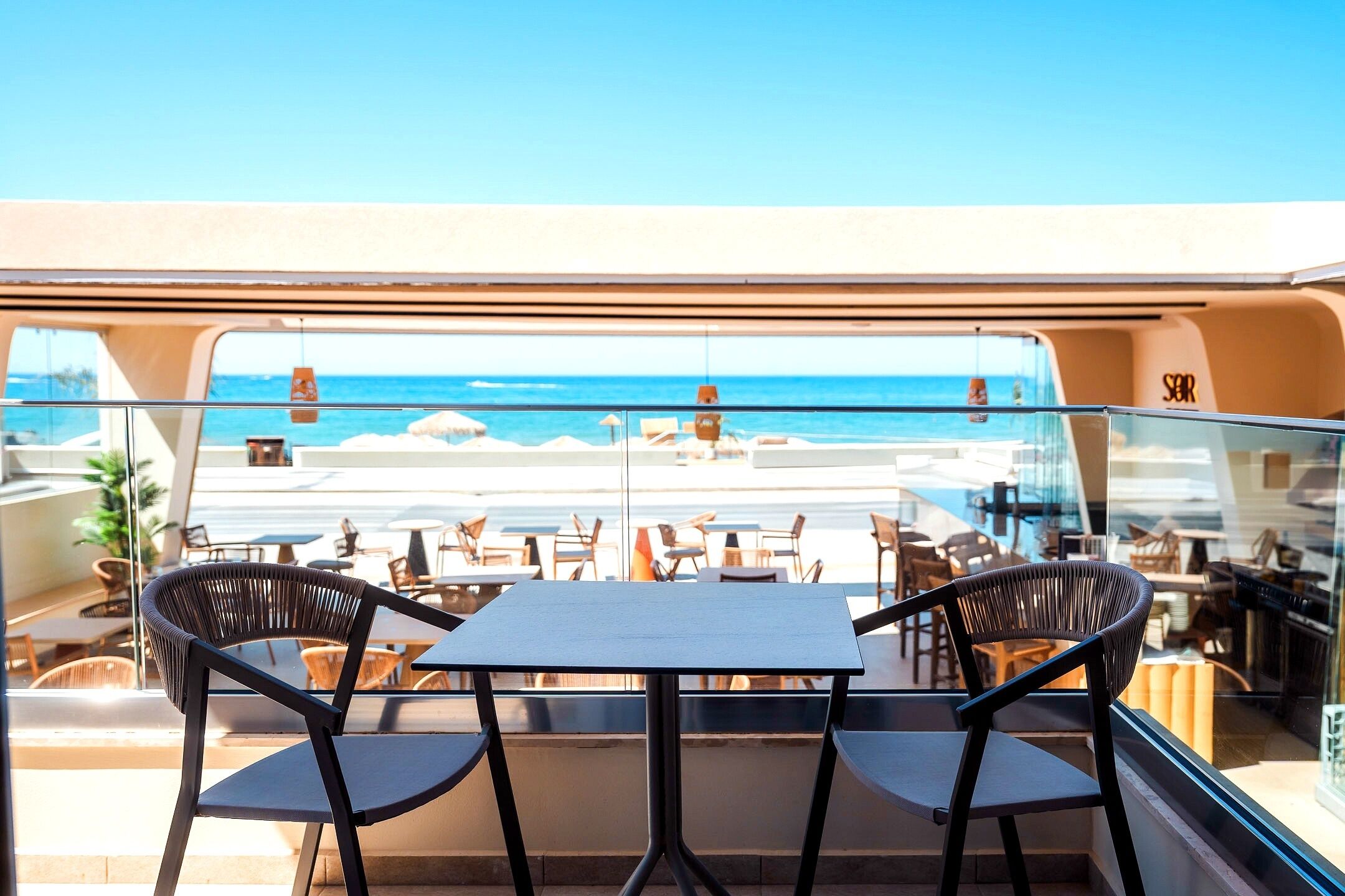 Un balcon avec une table et des chaises, donnant sur une plage et l’océan.