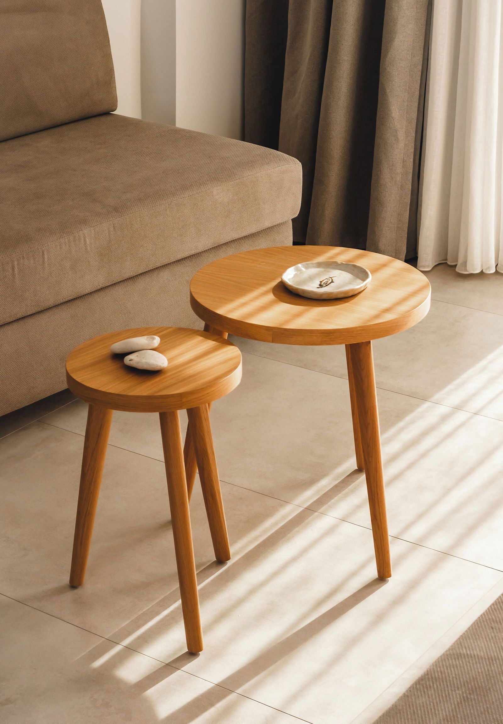 A modern living room with a beige sofa, two wooden side tables, and a white plate on one table.
