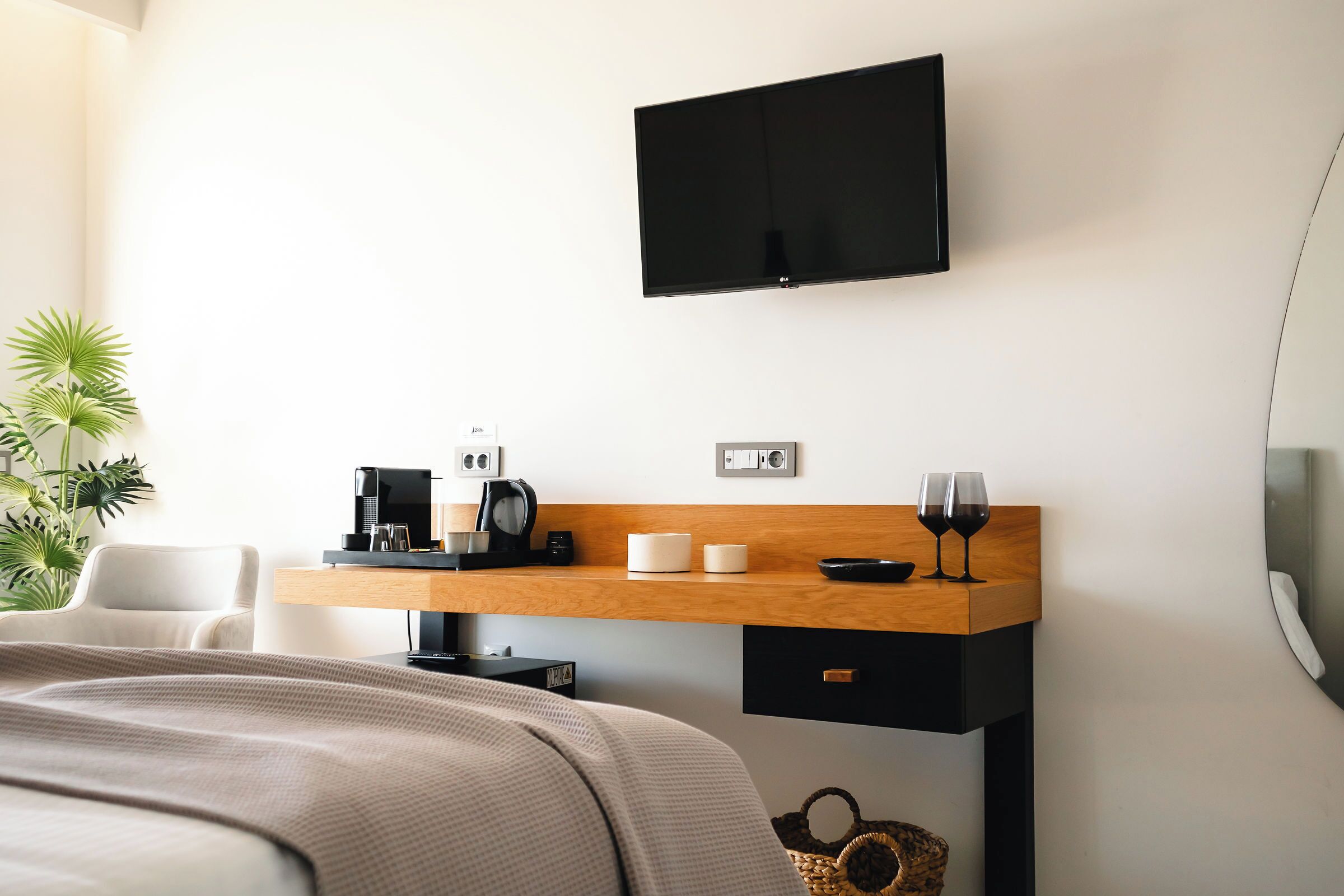 A hotel room with a bed, a desk with a coffee maker, a flat-screen TV, and a plant.