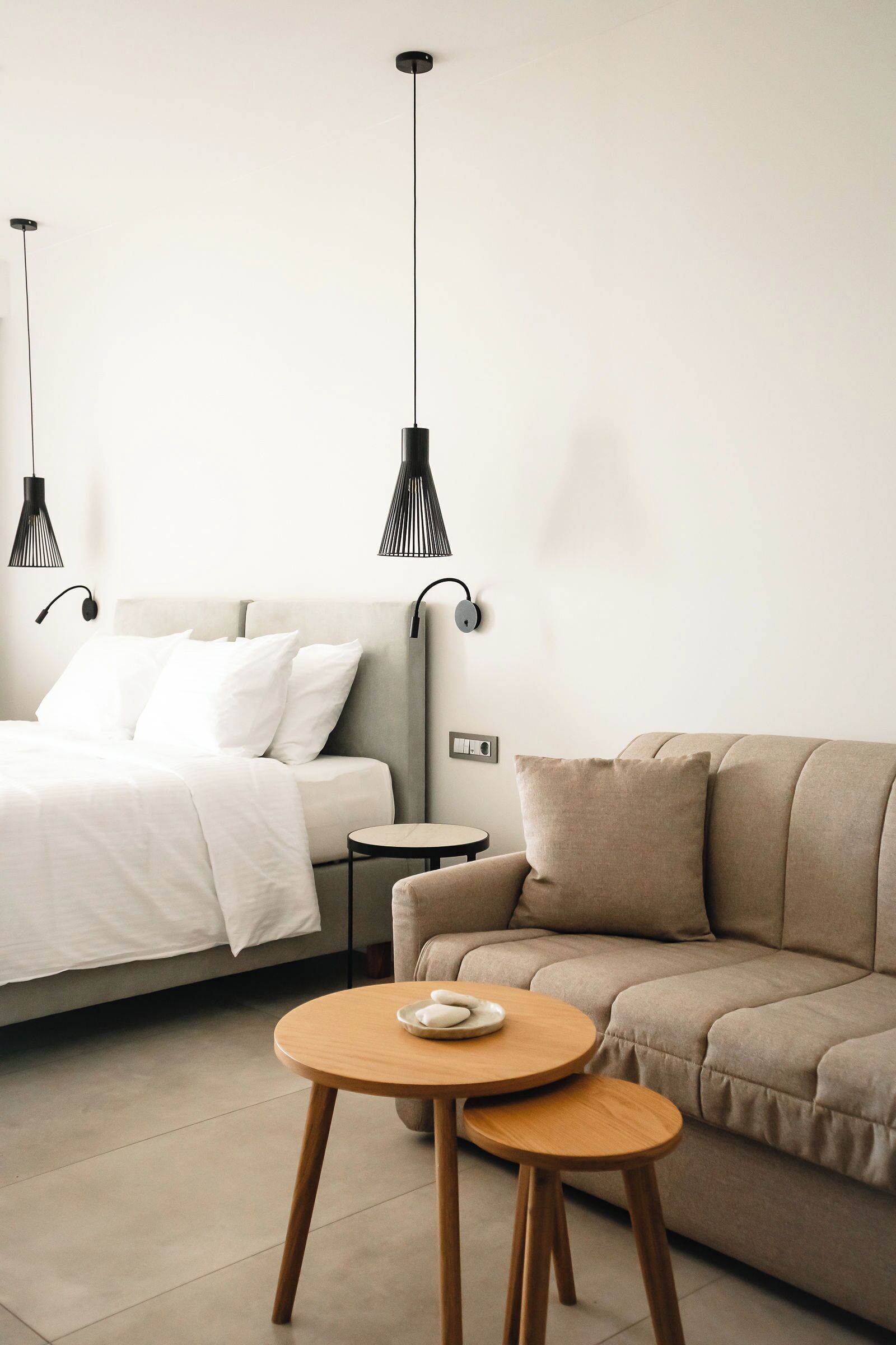 Ein modernes Schlafzimmer mit einem Bett, einer Couch, einem runden Holztisch und zwei Pendelleuchten.