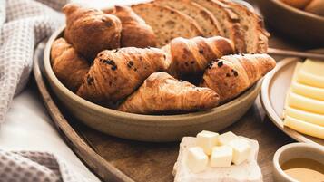 Uma bandeja de madeira com croissants, queijo e uma tigela de frutas.