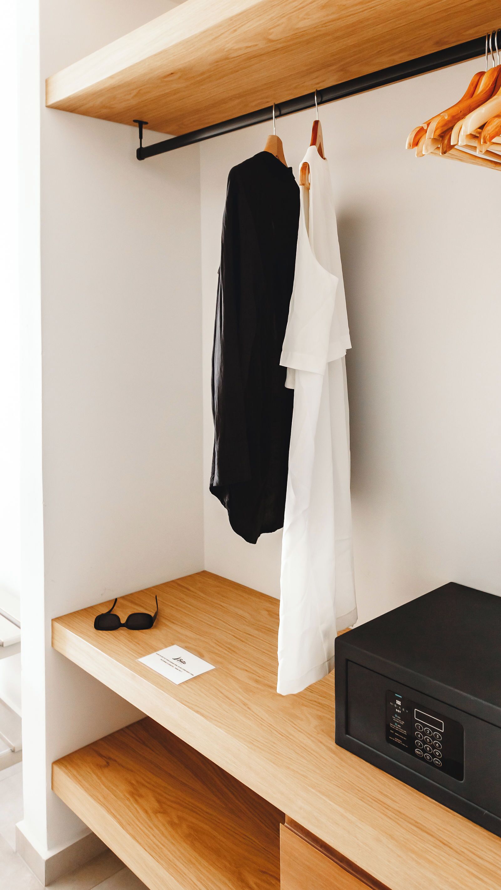 Ein Zimmer mit einem Holzbodenregal, einem schwarz-weißen Kleidungsstück, einer Sonnenbrille und einem schwarzen elektronischen Gerät.