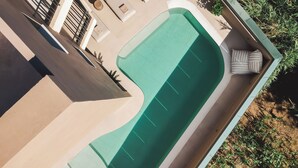 Vista aérea de una zona de piscina con sillones de descanso, una pequeña terraza y abundante vegetación.