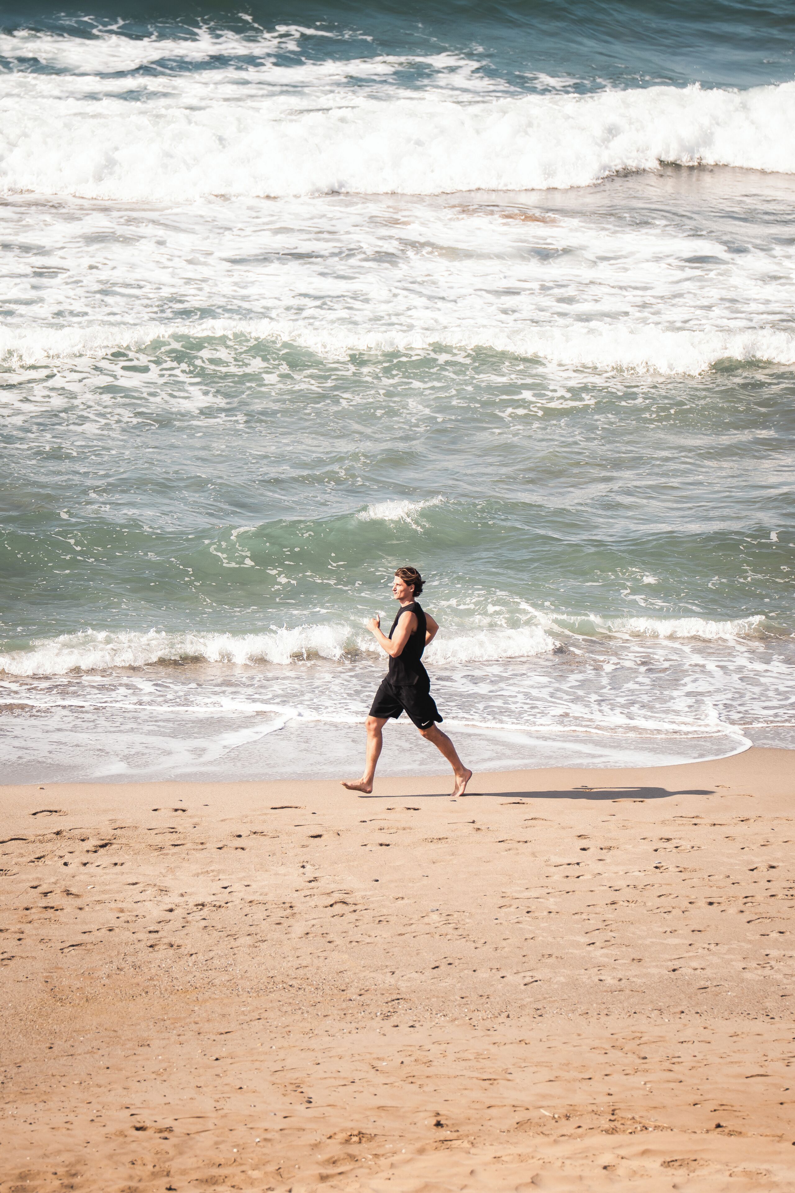 Uma pessoa caminhando numa praia de areia, com ondas ao fundo.
