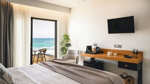 Una habitación de hotel moderna con una cama, un escritorio con televisor de pantalla plana, una silla, una planta pequeña y vista al océano.